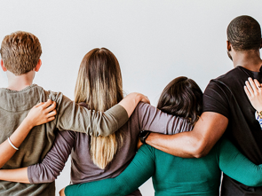 Four people standing side by side with their arms around each other's shoulders.