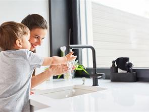 Adult and young child washing hands at a kitchen sink.