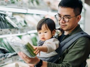 Adult holding a child while reading food packaging in a grocery store.