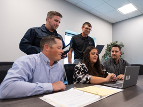 A group of colleagues gathered around a conference table collaborate on a laptop during a meeting in a modern office